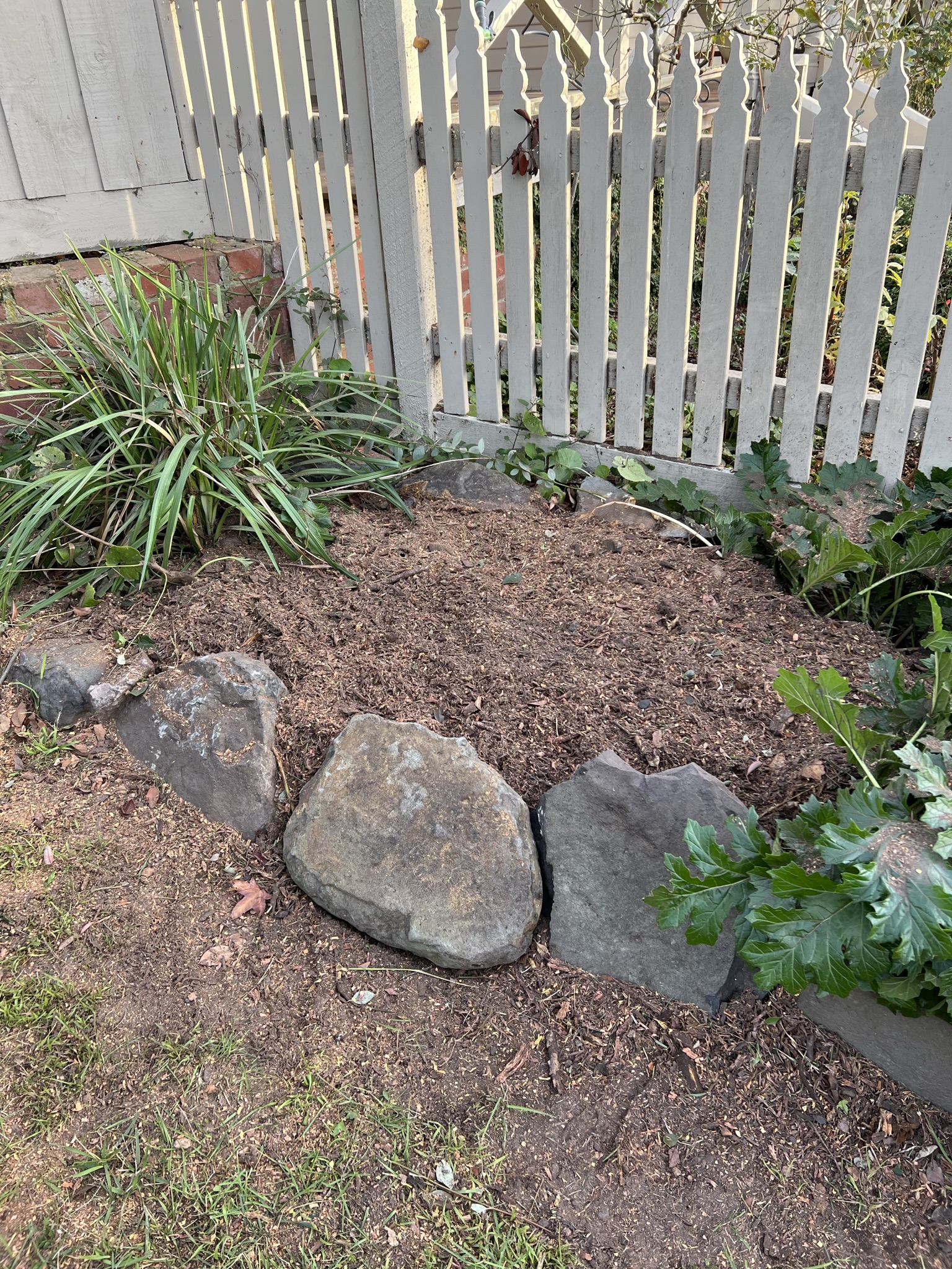 The same garden bed once the work is finished, raked level and covered in mulch, with the large border rocks replaced along its edge.